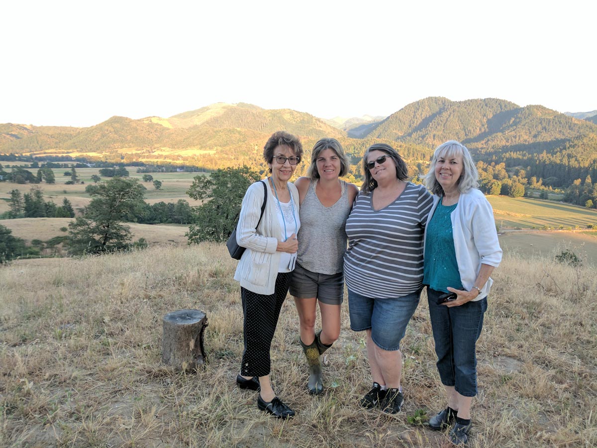Four women pose at the top of hill overlooking a beautiful valley